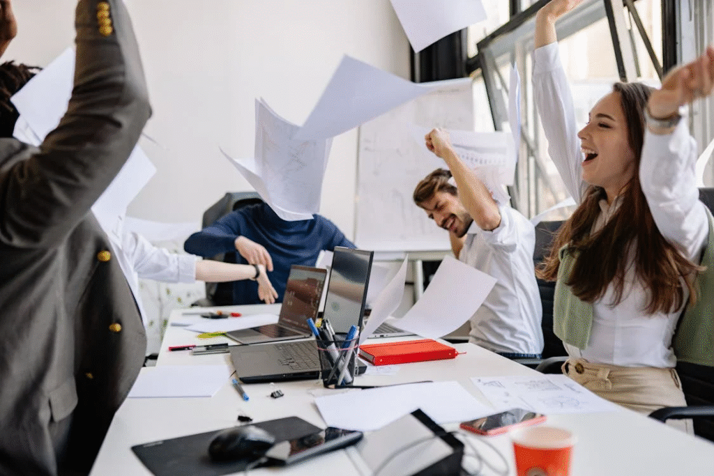 people in an office celebrating and throwing papers in the air while sitting around laptops and documents, showing the energy and joy of a meaningful career